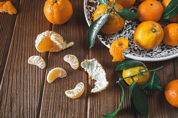 Fresh delicious mandarin oranges fruit or tangerines with green leaves in a bowl on wooden table