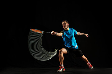 Young man playing badminton over black studio background. Fit male athlete isolated on dark with...