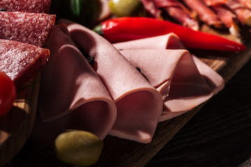 close up view of wooden cutting board with tasty sliced ham and vegetables