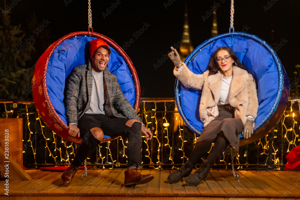 Wall mural Couple posing for funny photo on swing chair at Christmas market.