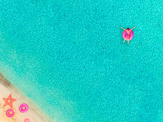 Fototapeta na wymiar Aerial view of woman floating on inflatable mattress by sandy beach.