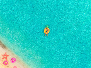 Aerial view of man floating on inflatable mattress by sandy beach.