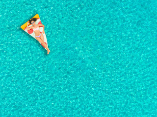 Aerial view of woman floating on inflatable pizza mattress, relaxing and smiling.