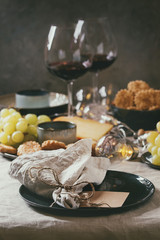 Home dinner table set with wine, cheese plate, appetizers and empty plate with cloth napkin.