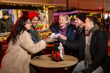 Group of friends cheering with traditional drink at Christmas market.