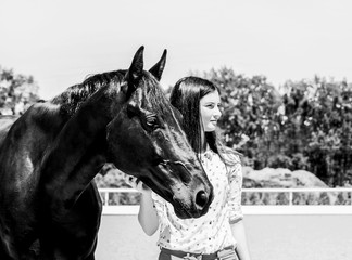 Girl and horse, black and white image of pretty young woman and gorgeous thoroughbred stallion. Fashion portrait of brunette model in equestrian uniform.
