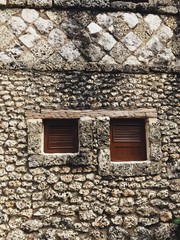 Background photo of antique-like wall made of light stone with two small windows with no glass. Stones have different textures and color. Windows are brown.