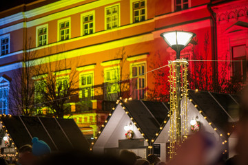 Crowded Christmas market in city center, decorated wooden huts with glowing lights. People enjoying event and searching for gifts. Beautiful Christmas background. 