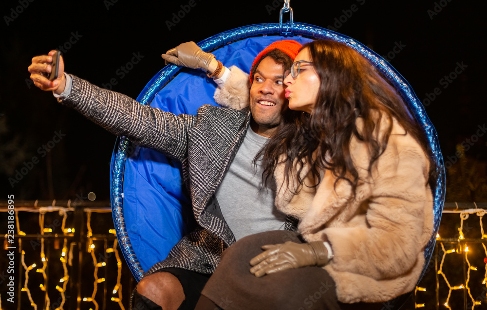 Wall mural Couple sitting on swing chair and taking selfie at Christmas market.