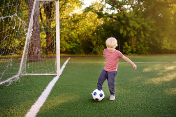 Little boy having fun playing a soccer/football game on summer day. Active outdoors game/sport for children.