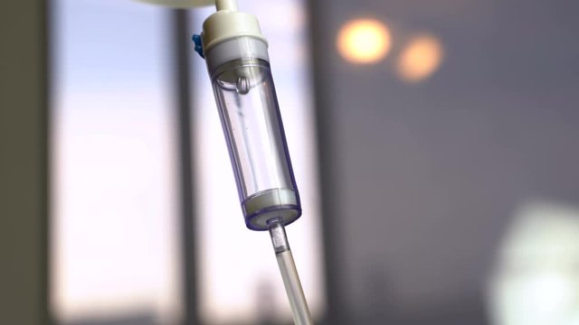 Macro shot of a hospital drop counter in a metallic case with dripping beads of saline in an intensive therapy room with clean white walls