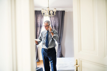 Mature businessman on a business trip standing in a hotel room, making phone call.