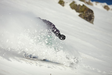 Snowboarder moves down the snowy slope raising a cloud of snow dust.