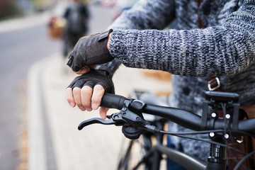 A close-up of a cyclist with electrobike putting on gloves outdoors in town.