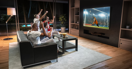 Group of students are watching a soccer moment on the TV and celebrating a goal, sitting on the...