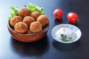 Falafel lies in a wooden plate. On the table lie tomatoes, cucumbers, lettuce, dill, lemon, sour...