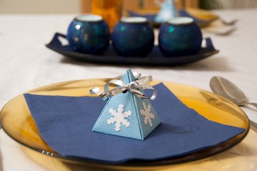 Christmas dinner table decoration. Blue gift box decorated with white snowflake and ribbon on the...