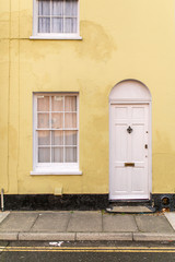 Fototapeta na wymiar Yellow and white typical english house facade with door and window viewed from outdoors.