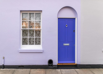 Typical english house facade with lavender color door and white window viewed from outdoors.