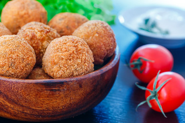 Falafel lies in a wooden plate. On the table lie tomatoes, cucumbers, lettuce, dill, lemon, sour cream.