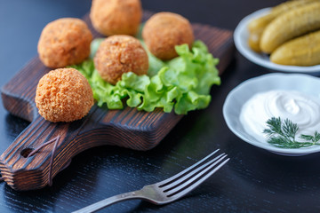 Falafel lies on a wooden cutting board. On the table lie tomatoes, cucumbers, lettuce, dill, lemon, sour cream.