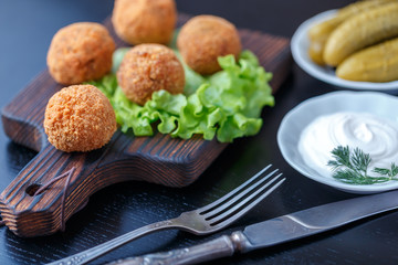 Falafel lies on a wooden cutting board. On the table lie tomatoes, cucumbers, lettuce, dill, lemon, sour cream.