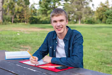 Happy teenager doing school work outdoors on a sunny afternoon.