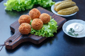 Falafel lies on a wooden cutting board. On the table lie tomatoes, cucumbers, lettuce, dill, lemon,...