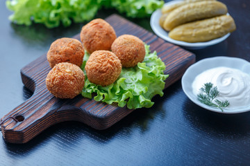 Falafel lies on a wooden cutting board. On the table lie tomatoes, cucumbers, lettuce, salad, dill, lemon, sour cream.