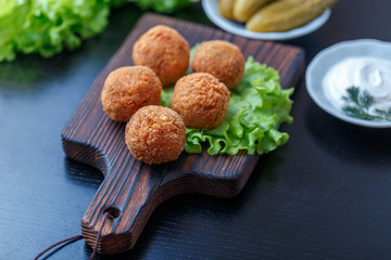 Falafel lies on a wooden cutting board. On the table lie tomatoes, cucumbers, lettuce, salad, dill,...