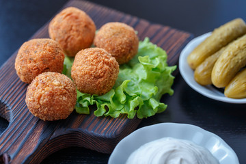 Falafel lies on a wooden cutting board. On the table lie tomatoes, cucumbers, lettuce, salad, dill, lemon, sour cream.