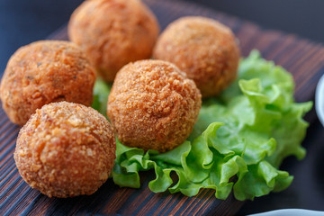 Falafel lies on a wooden cutting board. On the table lie tomatoes, cucumbers, lettuce, salad, dill, lemon, sour cream.