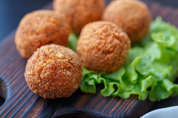 Falafel lies on a wooden cutting board. On the table lie tomatoes, cucumbers, lettuce, salad, dill, lemon, sour cream.