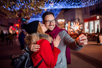 Young romantic couple is having fun with bengal lights in the winter city street.