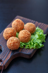 Falafel lies on a wooden cutting board. On the table lie tomatoes, cucumbers, lettuce, salad, dill, lemon, sour cream.