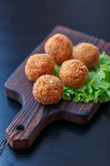 Falafel lies on a wooden cutting board. On the table lie tomatoes, cucumbers, lettuce, salad, dill, lemon, sour cream.