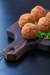 Falafel lies on a wooden cutting board. On the table lie tomatoes, cucumbers, lettuce, salad, dill, lemon, sour cream.