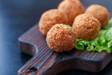 Falafel lies on a wooden cutting board. On the table lie tomatoes, cucumbers, lettuce, salad, dill, lemon, sour cream.