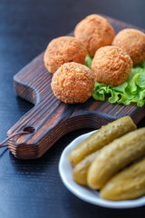 Falafel lies on a wooden cutting board. On the table lie tomatoes, cucumbers, lettuce, salad, dill, lemon, sour cream.