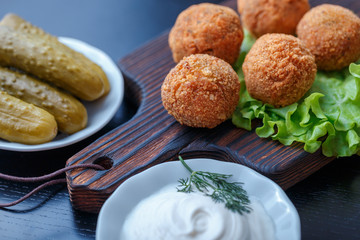 Falafel lies on a wooden cutting board. On the table lie tomatoes, cucumbers, lettuce, salad, dill, lemon, sour cream.