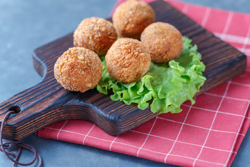 Falafel lies on a wooden cutting board. On the table lie tomatoes, cucumbers, lettuce, salad, dill, lemon, sour cream.