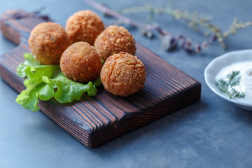 Falafel lies on a wooden cutting board. On the table lie tomatoes, cucumbers, lettuce, salad, dill, lemon, sour cream.