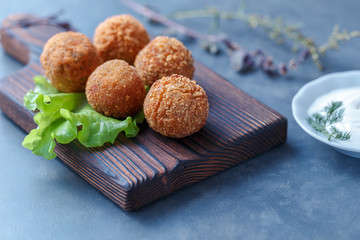 Falafel lies on a wooden cutting board. On the table lie tomatoes, cucumbers, lettuce, salad, dill, lemon, sour cream.