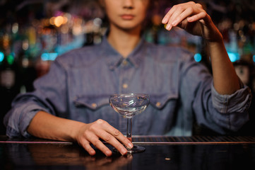 Female bartender holding an empty cocktail glass standing on the bar counter