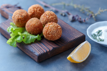 Falafel lies on a wooden cutting board. On the table lie tomatoes, cucumbers, lettuce, salad, dill,...