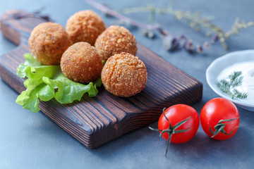 Falafel lies on a wooden cutting board. On the table lie tomatoes, cucumbers, lettuce, salad, dill,...