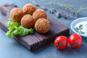 Falafel lies on a wooden cutting board. On the table lie tomatoes, cucumbers, lettuce, salad, dill,...