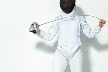 Young fencer athlete wearing fencing costume and mask holding the sword. Isolated on white...