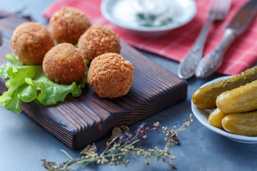 Falafel lies on a wooden cutting board. On the table lie tomatoes, cucumbers, lettuce, salad, dill, lemon, sour cream.