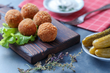 Falafel lies on a wooden cutting board. On the table lie tomatoes, cucumbers, lettuce, salad, dill, lemon, sour cream.